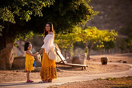 Mother and daughter enjoying a sunny walk under green trees.