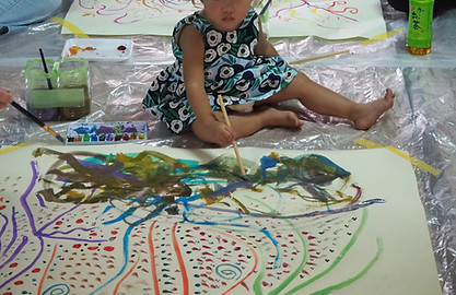 浄厳院アーティストinレジデンスの体験交流会で、床に広げた紙に筆で絵を描く赤ちゃん