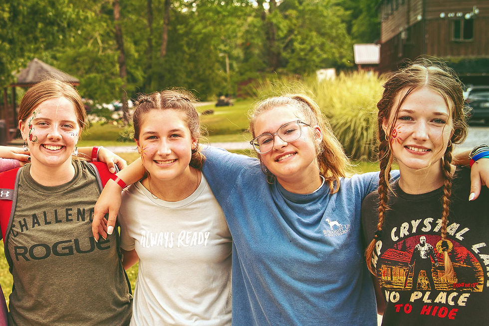 Girl campers with painted faces give hugs in a row.