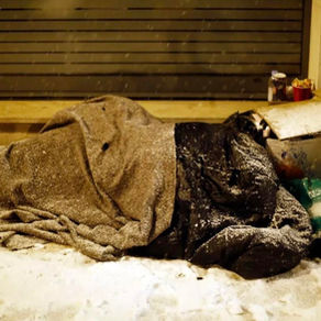 A homeless man sleeping on the pavement covered in snow.