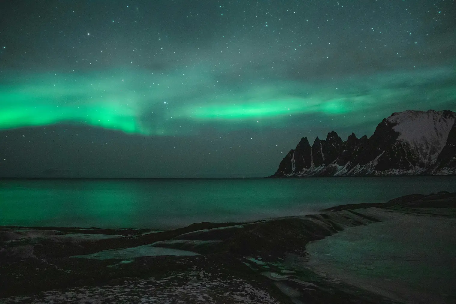 Picture of a night sky and sea illuminated by green glowing northern lights. by tobiasbjorkli