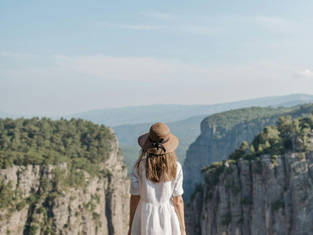 A person stands on a rocky cliff overlooking a calm ocean