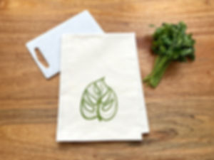 Flour sack kitchen towel on wood background with a stylized Monstera leaf printed in green ink