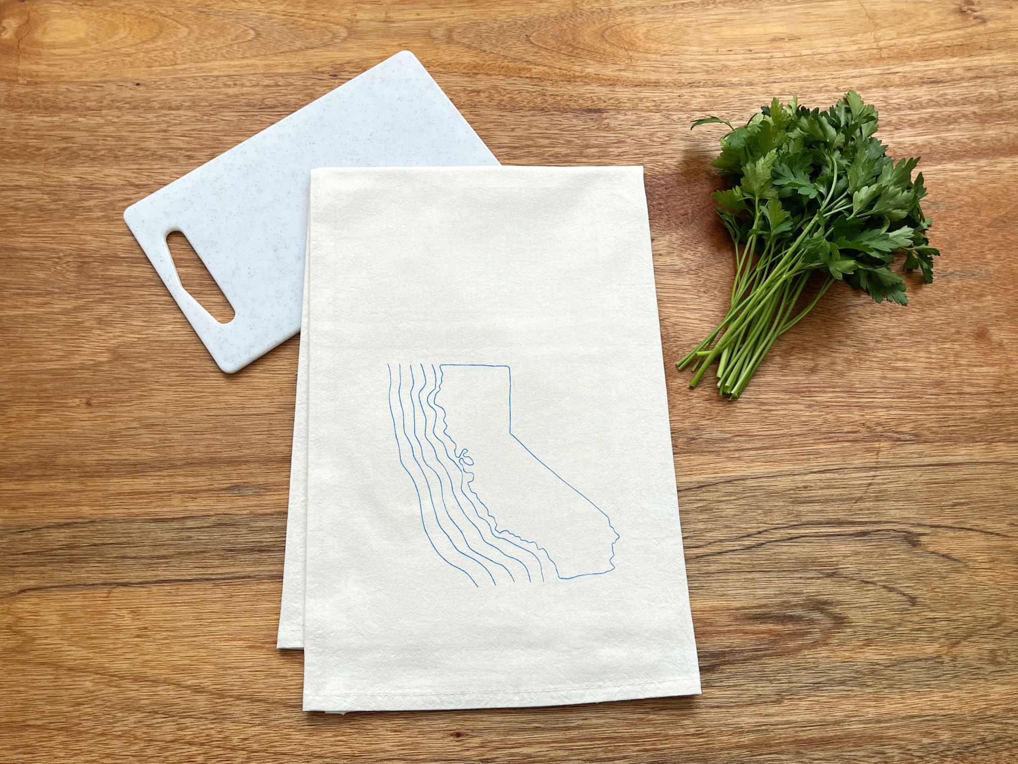 California state outline in light blue ink with waves off coastline on white cutting board with wood background