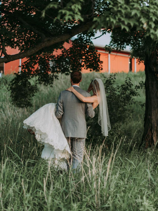 Groom carrying bride in grassy field