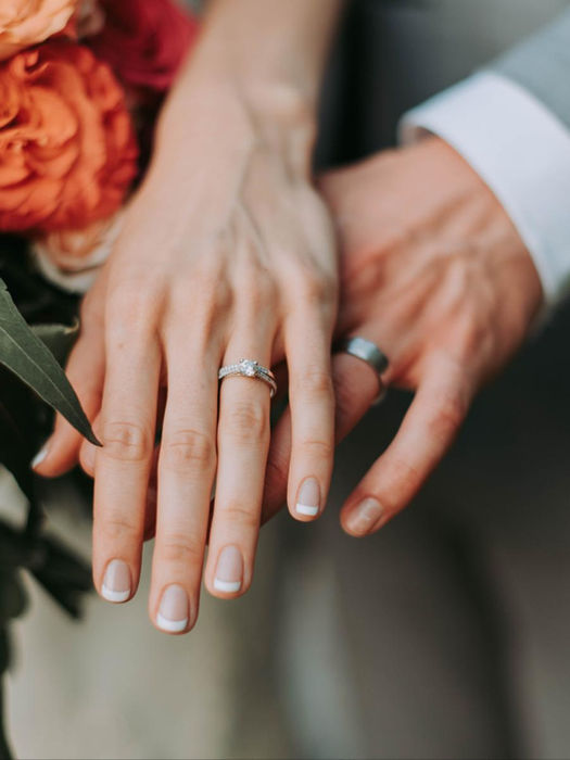 Joined hands with engagement and wedding rings, bouquet.