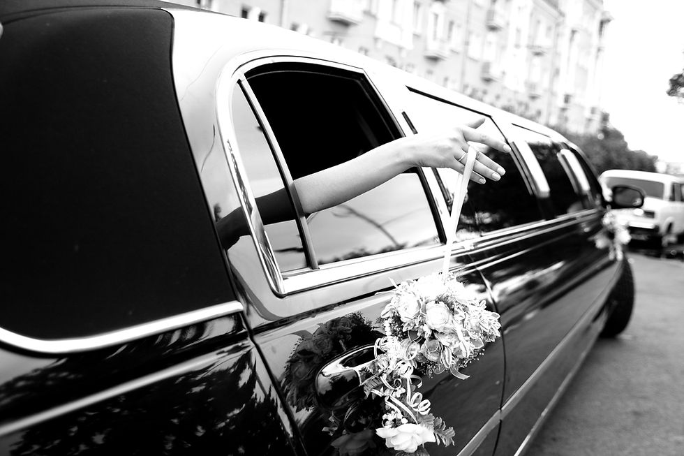 Black and white photo of a wedding limousine with a hand holding a bouquet out of the window
