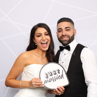 A bride and groom holding a just married sign in front of a grey and white backdrop