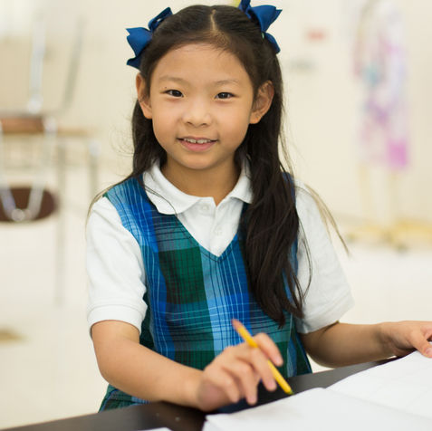 Female student smiling. Student in classroom setting. Smiling student working on workbook. Writing. ELA. English Language Arts. Chinese student. Diversity.