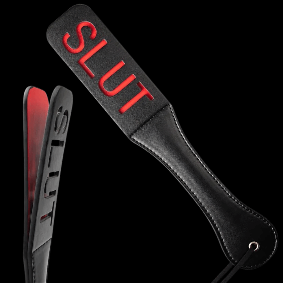 Black leather paddle with "SLUT" cut out revealing red beneath, set against a black background. Includes a handle loop.
