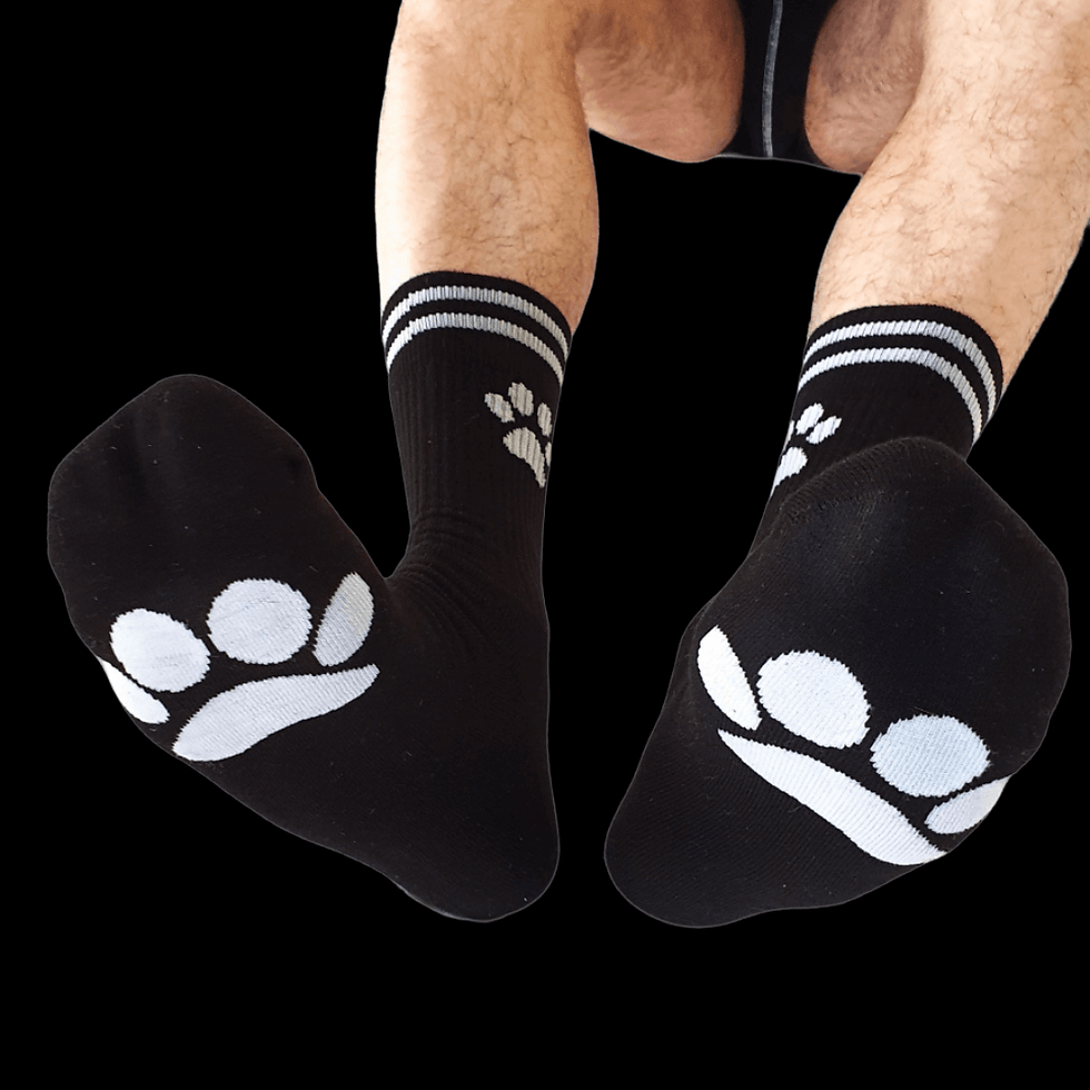 Person wearing black socks with white paw prints and stripes sits against a black background.