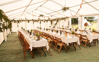 Tables dressées sous une tente blanche, des nappes blanches sont sur les tables et de la décoration florale également