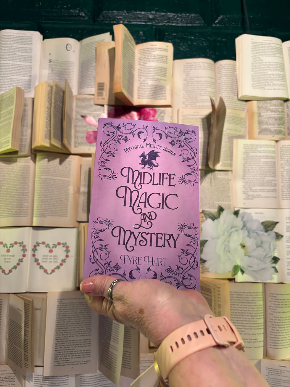 The fantasy book "Midlife, Magic & Mystery" by Fyre Hart being held out above several open books.