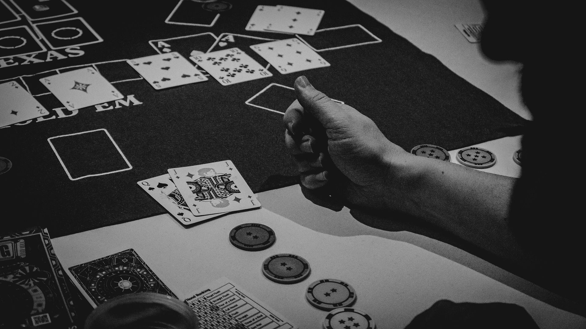 Black-and-white close-up of a HandyCon 15 attendee's hand rolling dice during a session of 'The Gang' board game, with cards and chips adding to the immersive tabletop experience.
