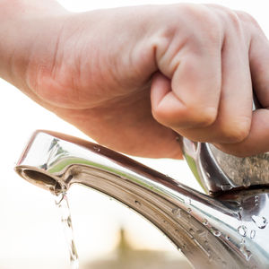 A decorative image of a person turning on a water faucet.