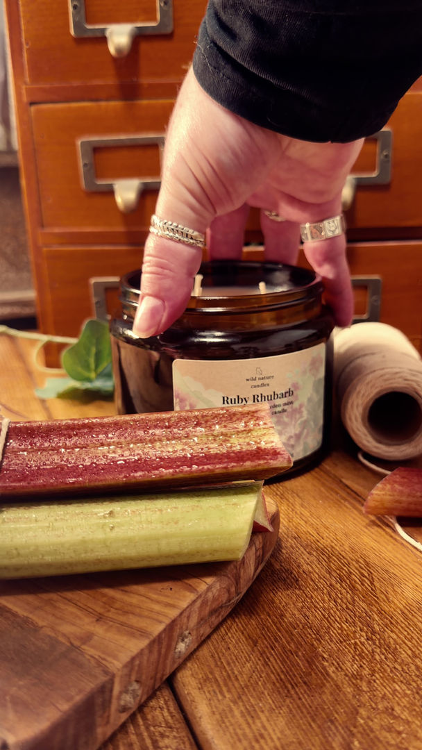 Thumbnail: A video of Ruby Rhubarb 3 wick soy candle on wooden board with fresh rhubarb and greenery, garden-inspired home fragrance