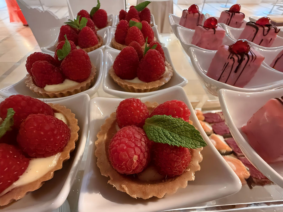 Himbeer-Tartelettes und rosa Gebäck auf weißen Tellern.