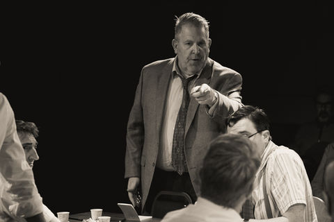 An image from the play 12 Angry Men. One juror is standing and pointing at other jurors around a table.