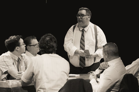 An image from the play 12 Angry Men. A juror stands, addressing the group with a few other jurors visible.