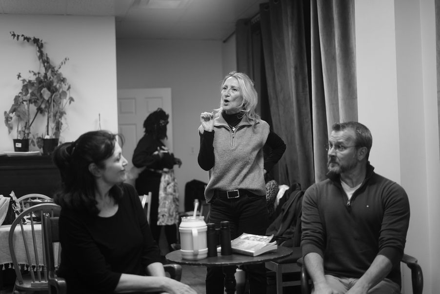 An image from rehearsals for the play "Vanya and Sonia and Masha and Spike". Two actors (Sonia and Vanya) are seated at a table looking at each other. A third female actor (Masha) is standing, apparently mid-sentence.