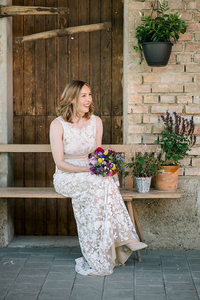 Braut in Boho Spitzenkleid lacht und hält ein Blumenstrauß