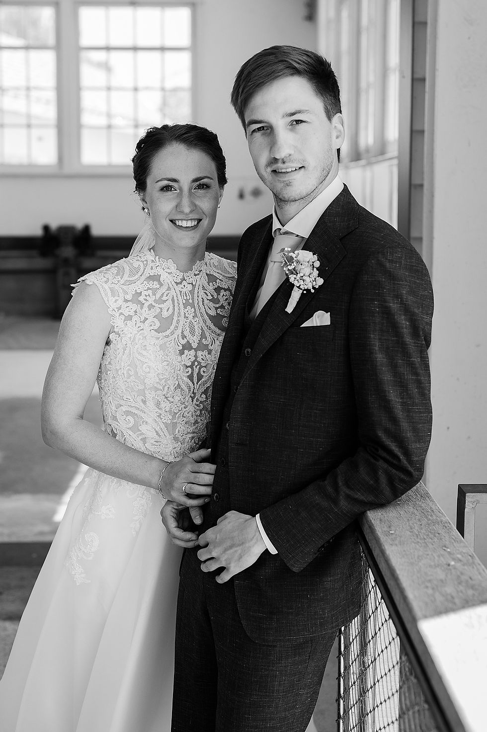 Braut in Brautkleid trägt Schleier, Bräutigam schaut in die Kamera