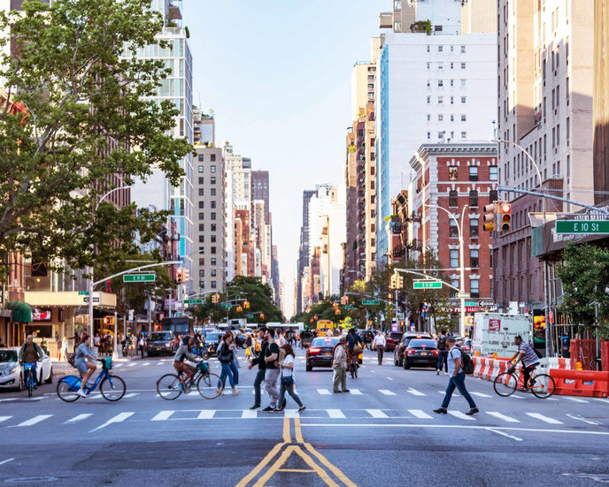 People riding bikes and crossing a road in a busy city.