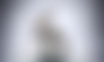 Man in suit struggles to balance on an oversized bear trap in a gray room. He looks worried, arms flailing for stability.