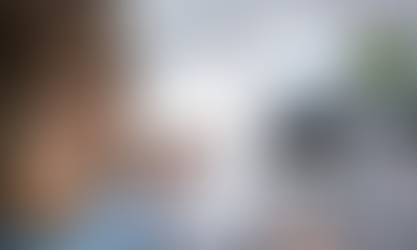 A person focuses on calculating finances with a calculator and an invoice, surrounded by a stack of receipts and a small plant.