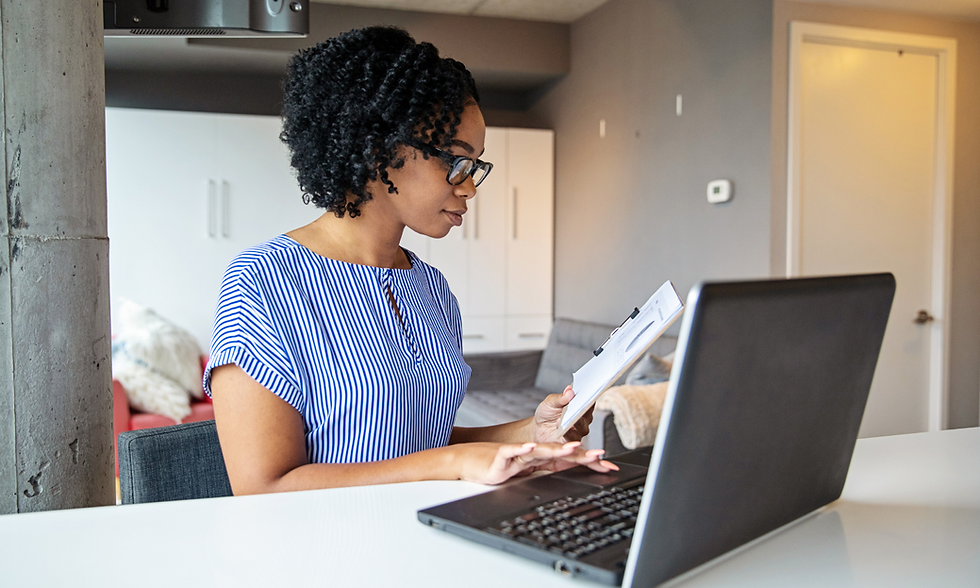 A focused woman works diligently from home, reviewing documents and typing on her laptop.