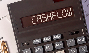Calculator displays "CASHFLOW" in bold letters. Background shows paperwork and a gold pen, suggesting financial analysis.