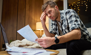 A concerned man studies his finances, looking stressed while reviewing bills at home.