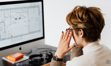 An architect deeply focused on reviewing detailed blueprints on her computer, surrounded by essential tools and equipment.