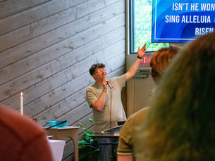 A worship leader in a tan shirt raising their hand in praise