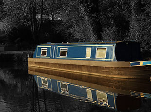 Canal barge narrow boat reflected in water surrounded by trees in late evening sunlight with selective color