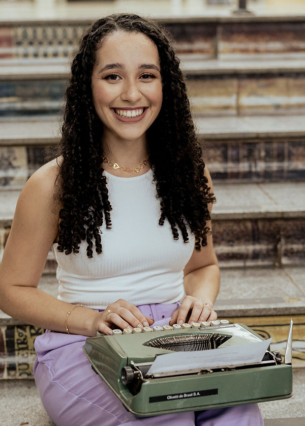 Mulher de cabelo cacheado sorrindo e segurando uma máquina de escrever