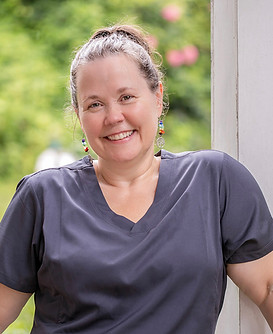 Smiling woman in grey scrubs standing on a porch