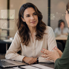 Mulher profissional em ambiente corporativo conversa com uma colega em uma mesa de trabalho, com notebook aberto e elementos gráficos digitais sutis sobrepostos à cena. A imagem transmite um contexto de RH, tecnologia e valorização das relações humanas no ambiente de trabalho.