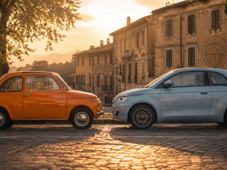 Fiat 500 clássico laranja e Fiat 500 elétrico moderno estacionados frente a frente em uma rua histórica italiana ao entardecer, com luz dourada e o logo GIRO500 discretamente integrado à fachada ao fundo.