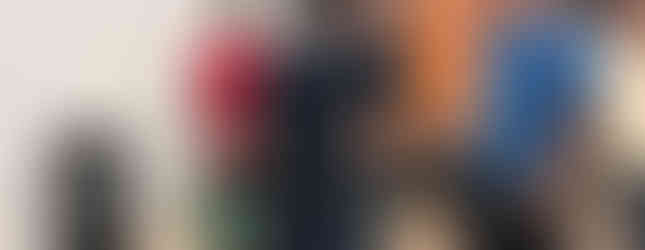 Participants gathered inside a workshop during an off-road event, talking next to display tires with aggressive tread. In the background, an orange Genius Tyres trailer, while the group checks out the gear in a relaxed, hands-on, technical vibe.