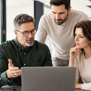 Três profissionais analisam juntos um conteúdo em um notebook, em um escritório moderno e iluminado, representando aprendizado, troca de experiências e colaboração no ambiente de trabalho.