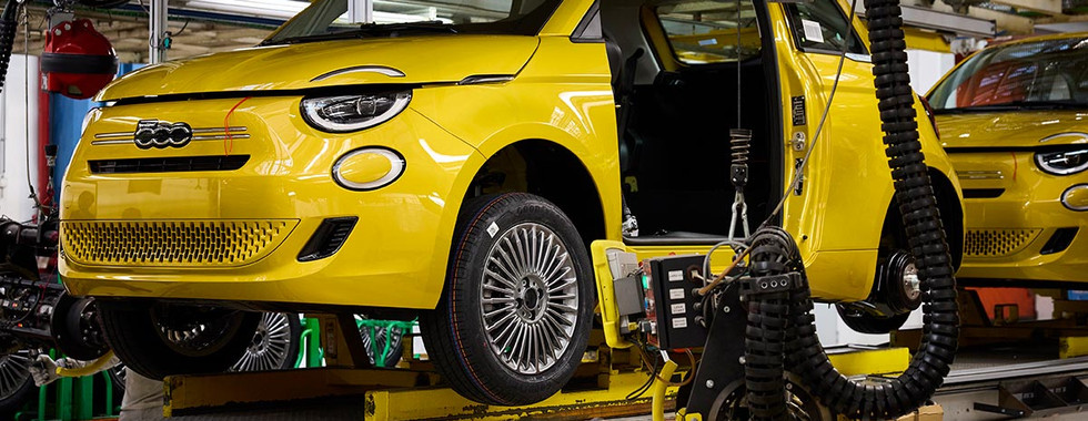 Fiat 500 Hybrid na linha de produção da fábrica de Mirafiori, em Torino, durante a montagem final com o veículo elevado para instalação de componentes e acabamento, evidenciando o processo industrial Made in Italy.