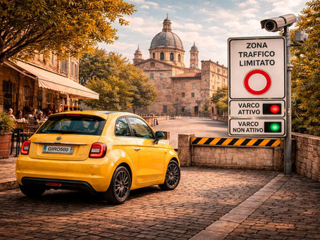Fiat 500e amarelo parado diante de uma placa de Zona a Traffico Limitato (ZTL) em um centro histórico italiano, com câmera de fiscalização ativa, rua de paralelepípedos e edifícios históricos ao fundo sob luz de fim de tarde.