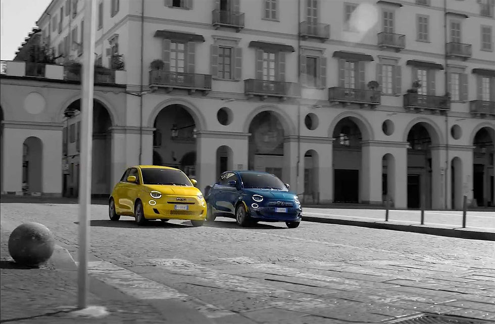 Dois automóveis Fiat 500 híbridos — um amarelo e um azul — estacionados numa praça histórica italiana com pavimento em pedra e arcadas clássicas ao fundo, numa fotografia a preto e branco com os carros em cor.