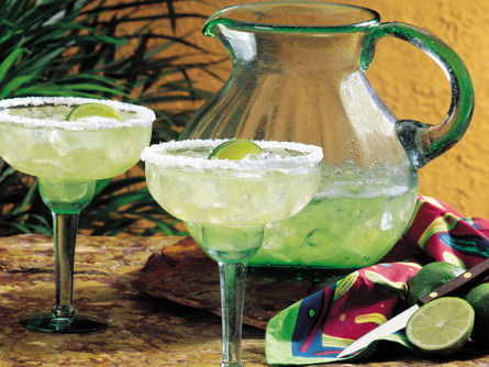Two glasses of margaritas with salted rims in front of a large pitcher.