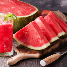 A glass of watermelon aqua fresca on a table with watermelon slices.