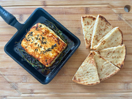 olden baked cheese in a black skillet with thyme beside toasted pita wedges on a wooden cutting board