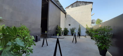 Outdoor event space with tables, plants, and a backdrop on a sunny day.
