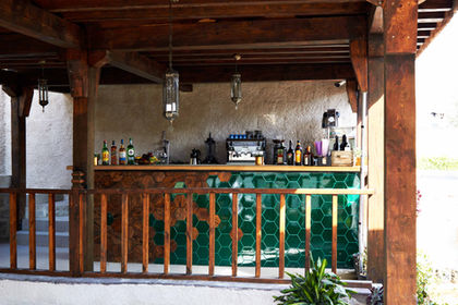 Bar with bottles and espresso machine, green tile, wooden fence, outdoor setting