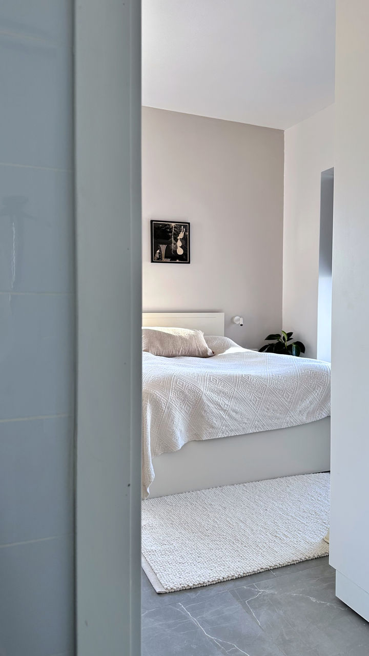 חדר שינה עם מיטה זוגית עם כיסוי לבן וקיר אפור ותמונה